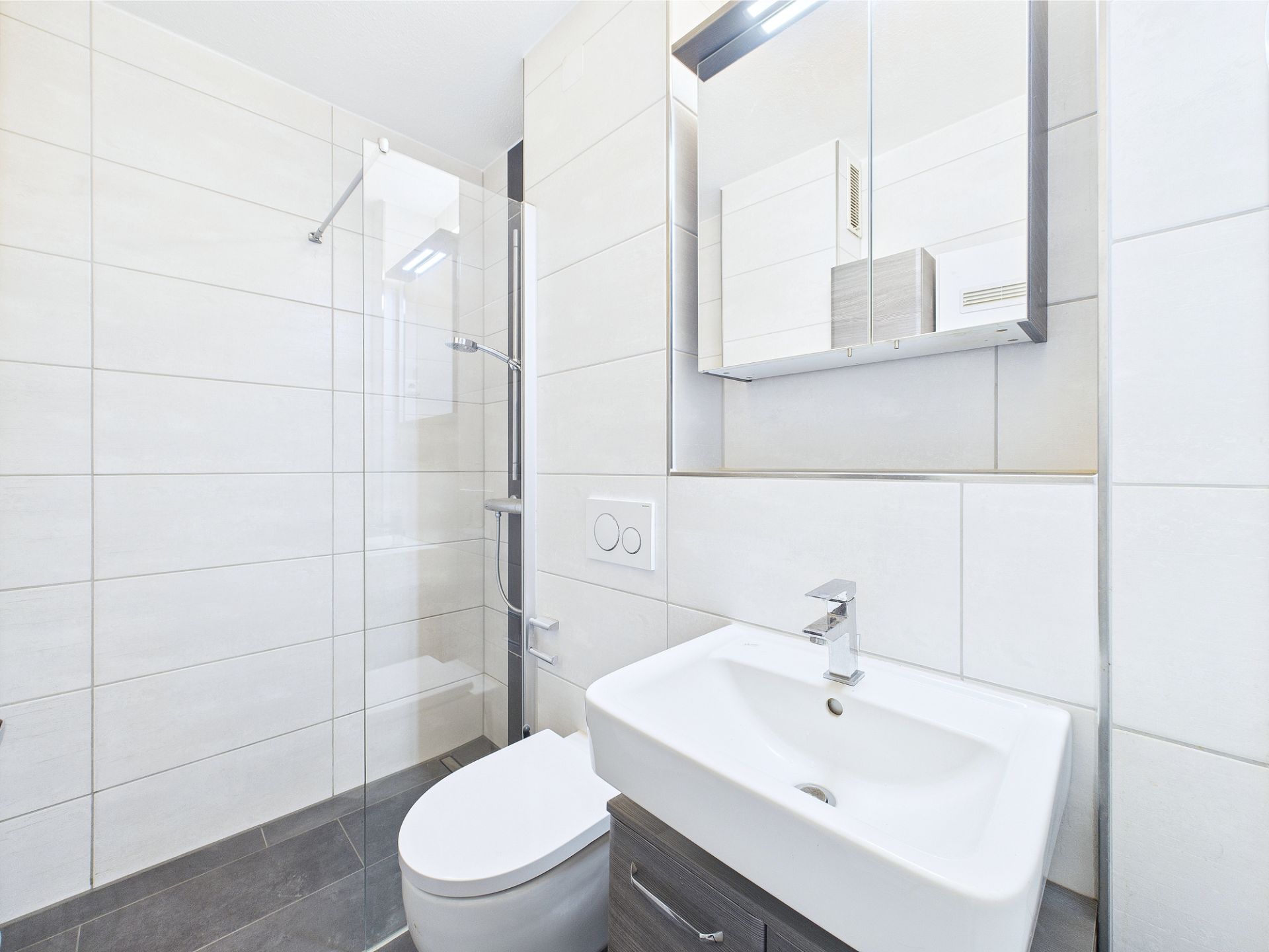 Modernes Bad mit Dusche, Waschbecken, Toilette und Spiegelschrank.