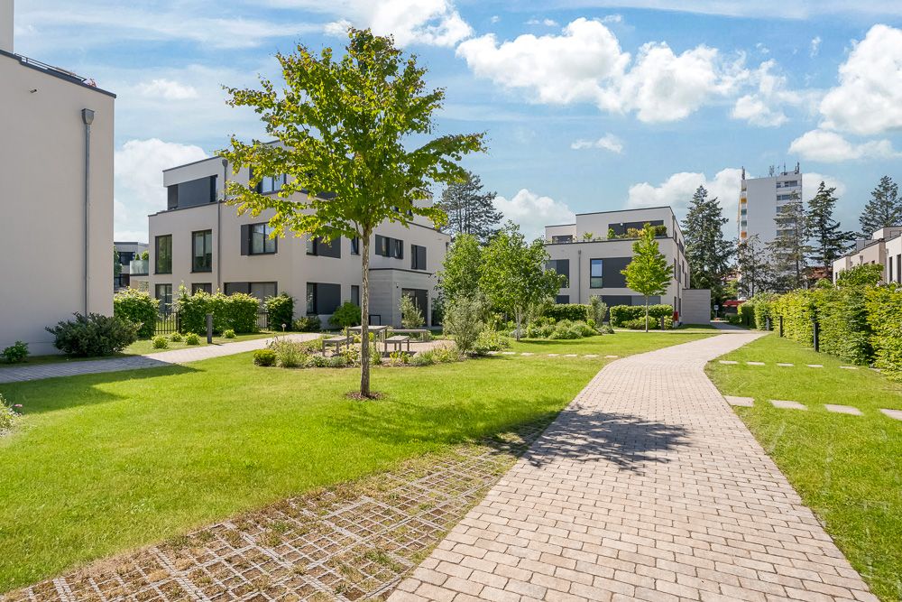 Moderner Wohnhof mit Gehweg, Rasenflächen, Bäumen und mehreren mehrstöckigen Wohnhäusern.