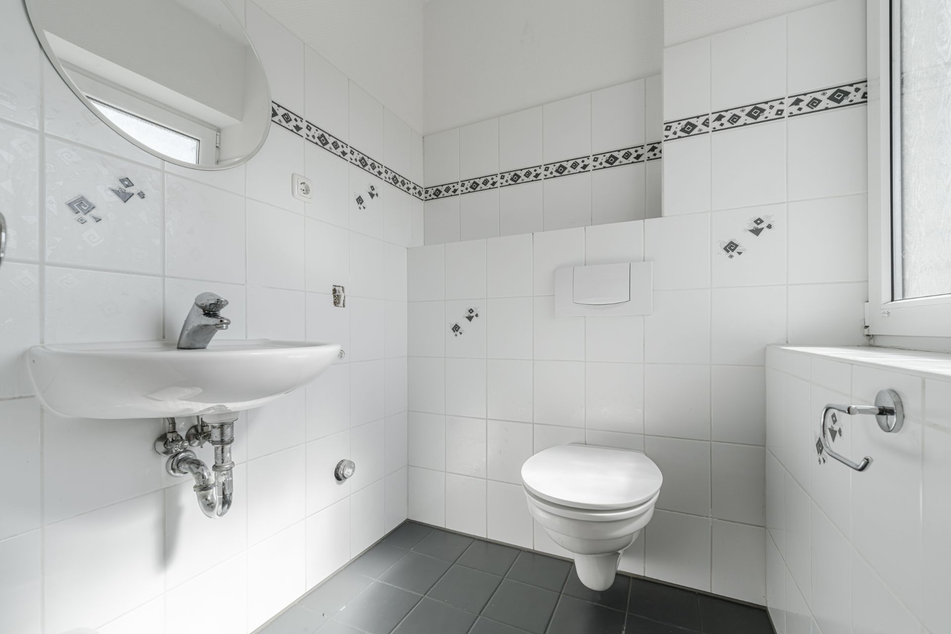 Helles Badezimmer mit Wandtoilette, Waschbecken, Spiegel und weiß gefliesten Wänden.