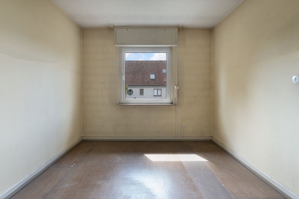Leerer Raum mit einem Fenster, beige Wänden und braunem Boden.