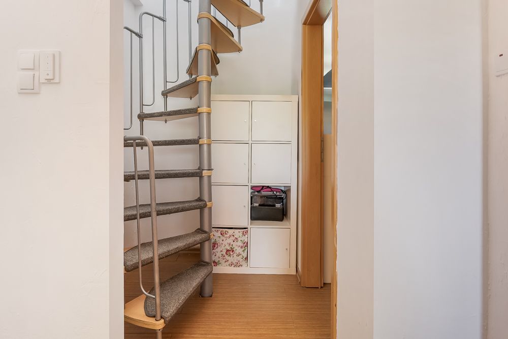 Wendeltreppe neben weißen Schränken in einem Flur mit Holzboden.