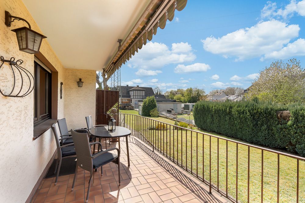 Überdachte Terrasse mit Tisch, vier Stühlen und Blick in einen gepflegten Garten.