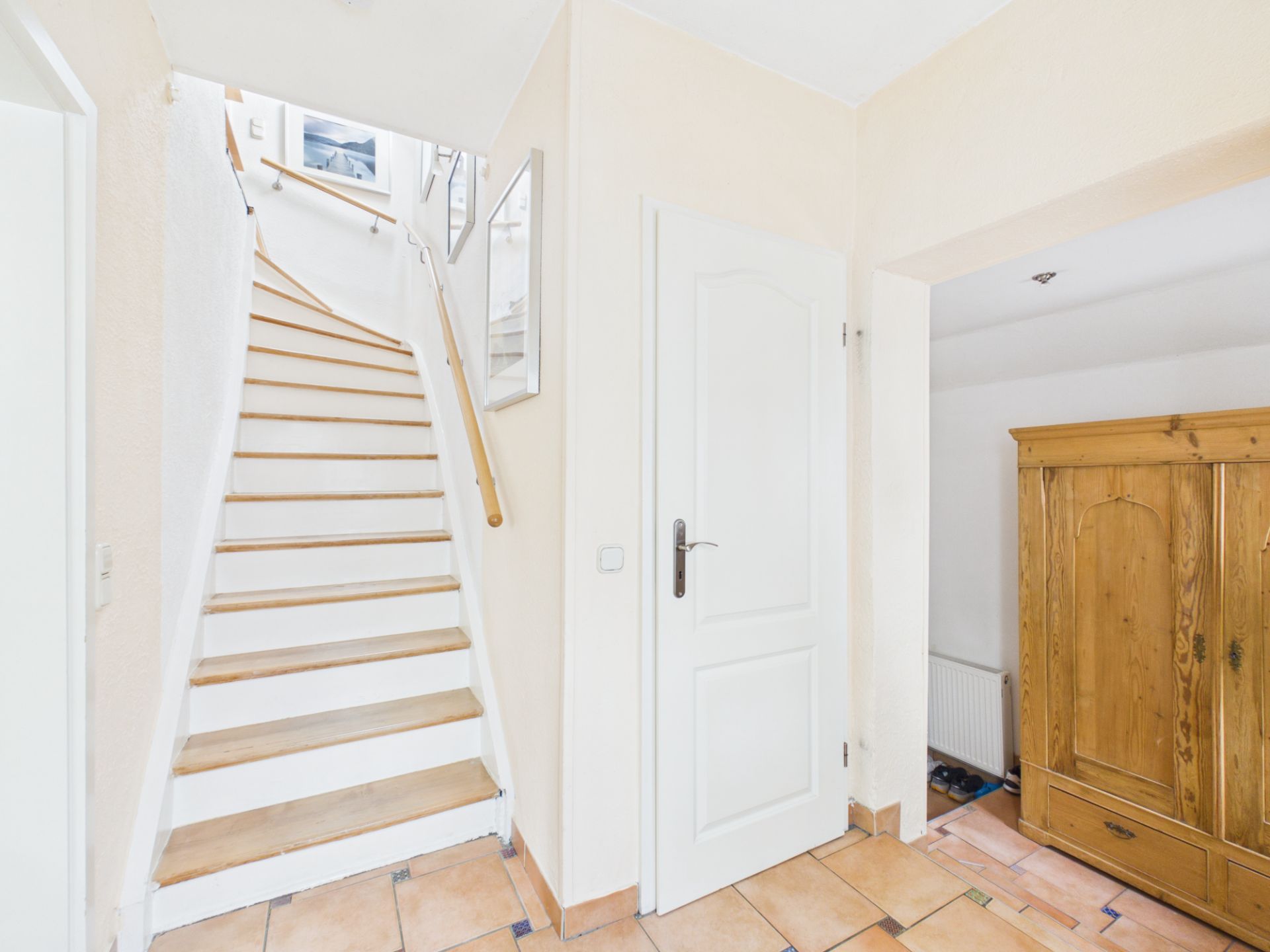Heller Flur mit Treppe, weißer Tür und großem Holzschrank.