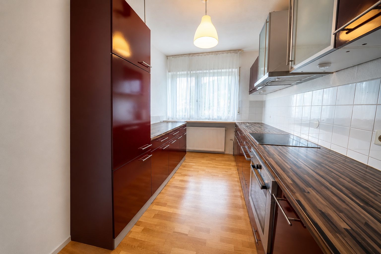 Moderne Küche mit Holzfußboden, roten Schränken und großem Fenster mit Gardine.
