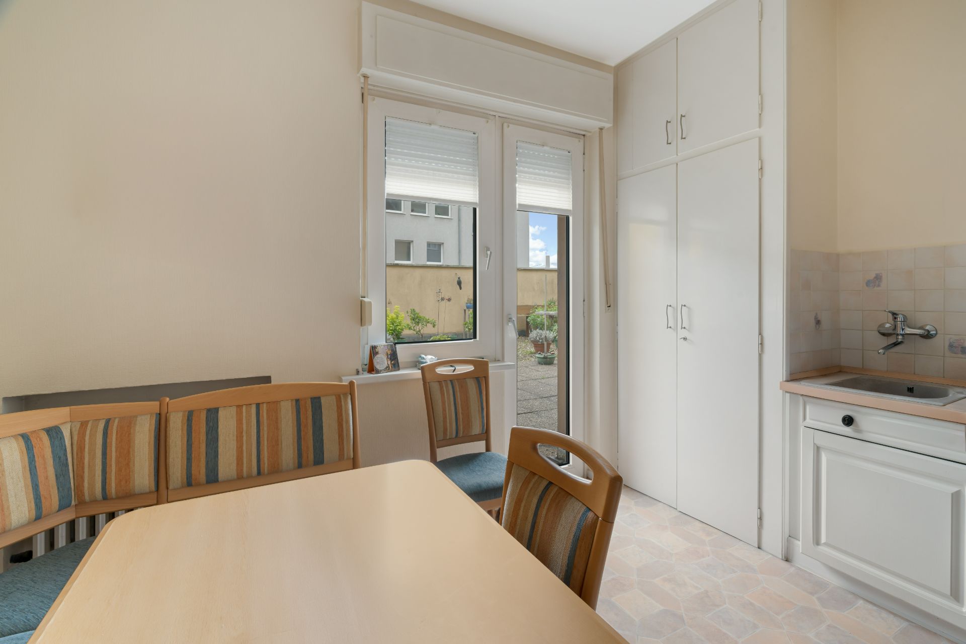 Essbereich mit Eckbank, Tisch, Stühlen und Blick auf Terrasse, daneben Küchenschrank und Spüle.
