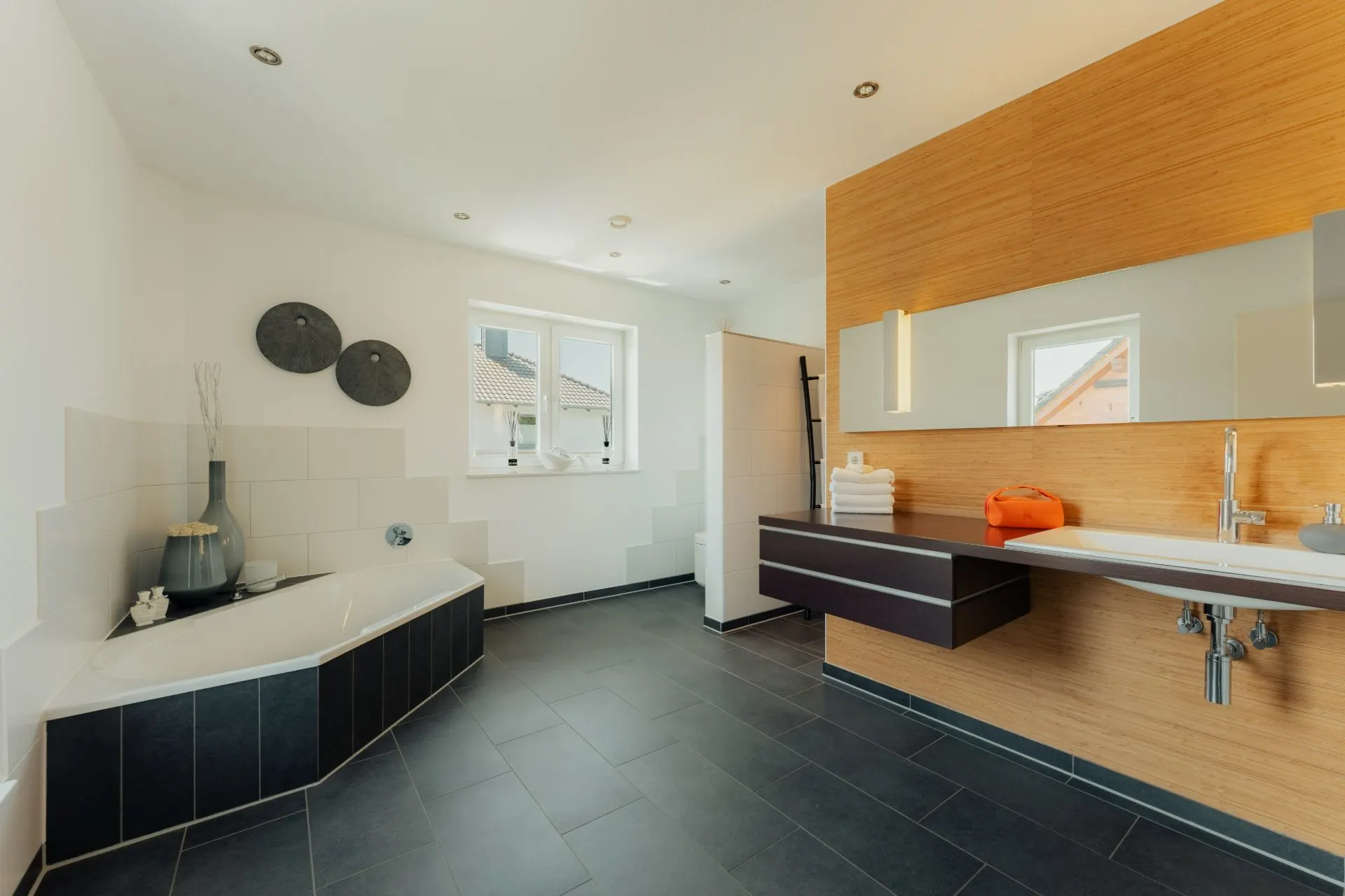 Modernes Badezimmer mit Eckbadewanne, großem Waschbecken, Spiegel und zwei Fenstern.