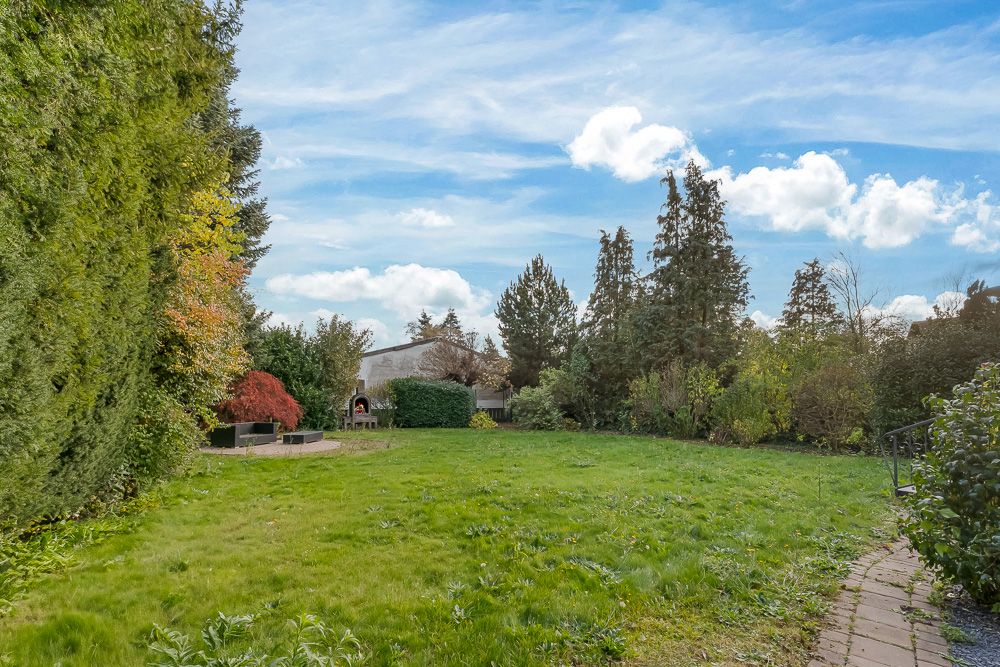 Großer Garten mit Rasenfläche, Terrasse, Bäumen und Sträuchern an einem sonnigen Tag.