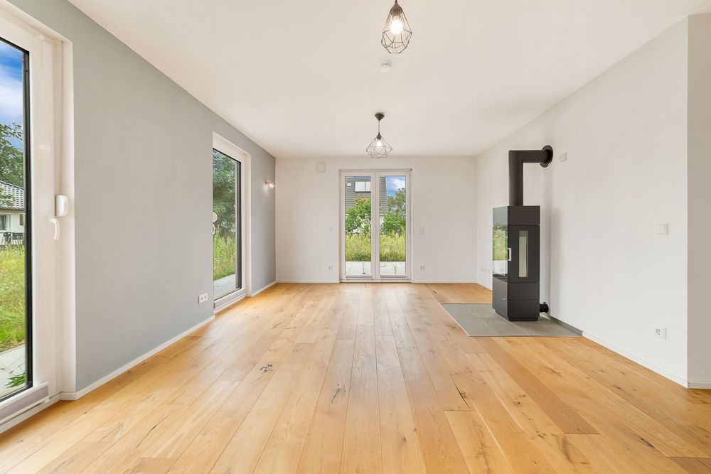 Helles Wohnzimmer mit Holzboden, Kamin und großen Fenstern mit Blick ins Grüne.