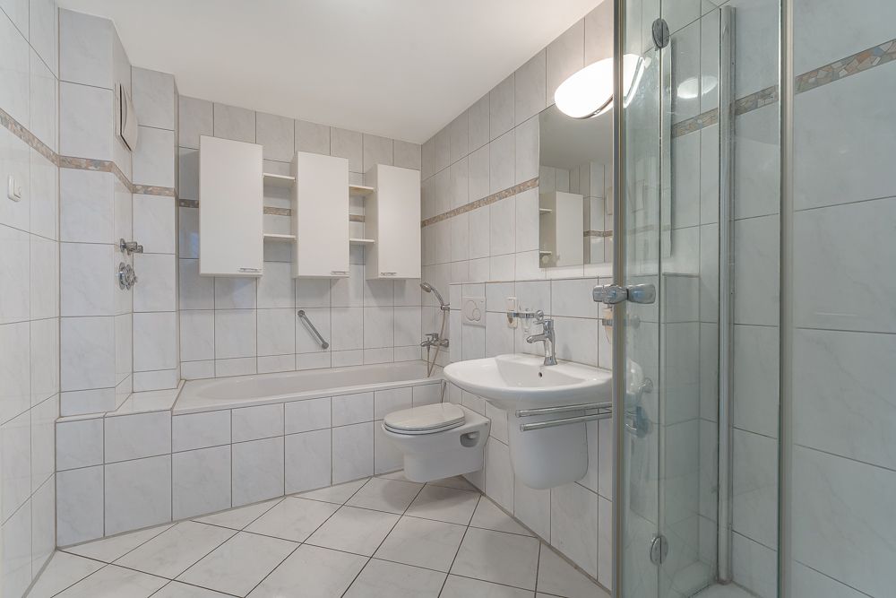 Modernes, hell gefliestes Badezimmer mit Dusche, Badewanne, Waschbecken und WC.