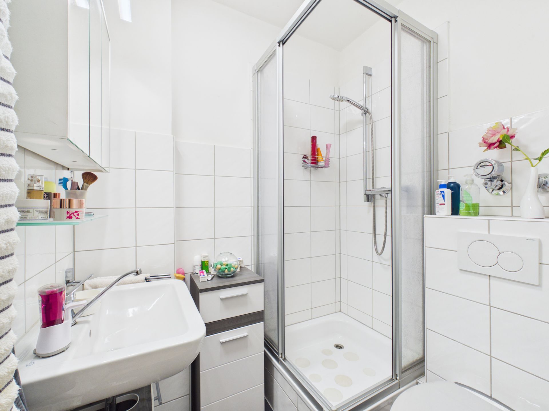 Helles Badezimmer mit Dusche, Waschbecken, Toilette und weißen Fliesen.