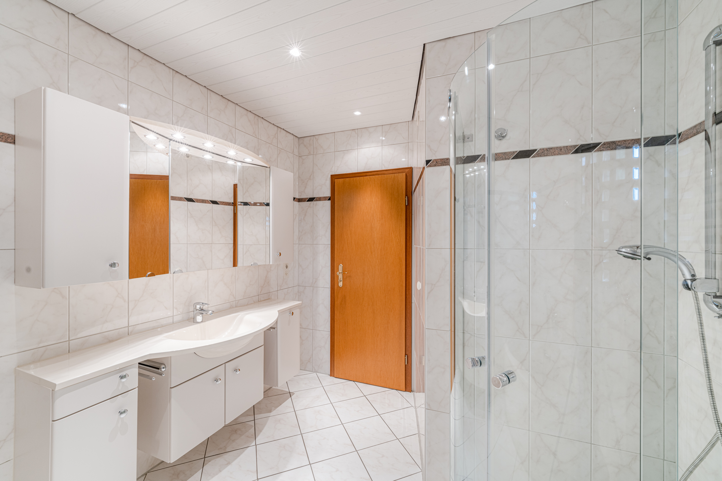 Modernes Badezimmer mit großer Dusche, Waschtisch, Spiegel und weißen Fliesen.