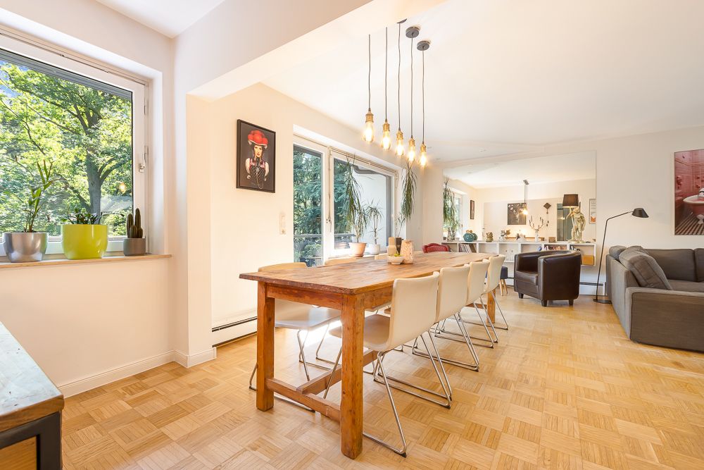Heller Wohn- und Essbereich mit Holztisch, weißen Stühlen und großen Fenstern mit Blick ins Grüne.