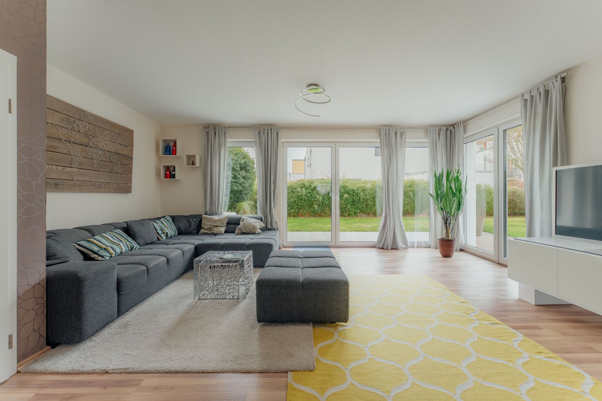 Helles Wohnzimmer mit großer grauer Sofaecke, Glastisch, Fernseher und gelbem Teppich.