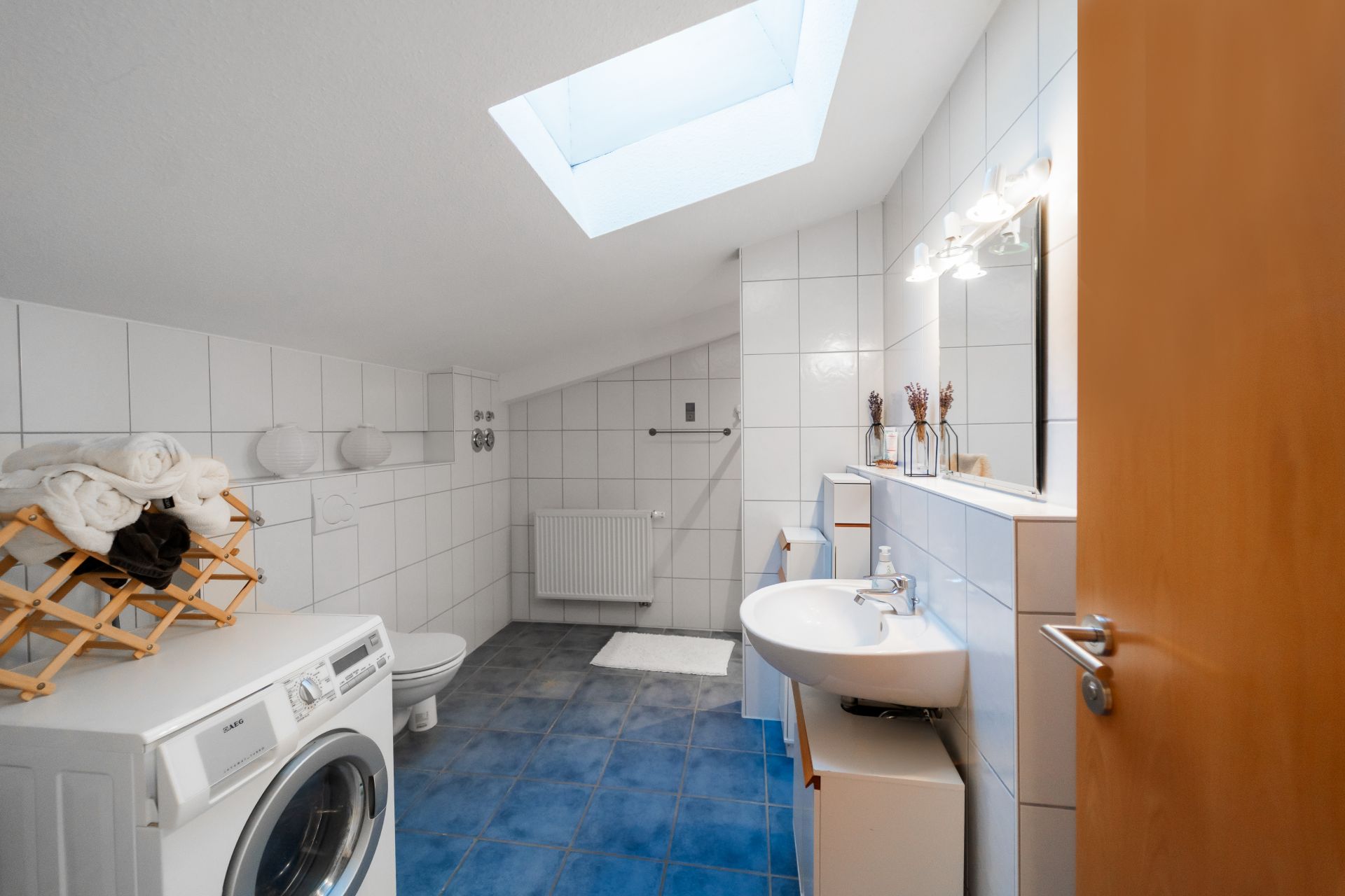 Helles Badezimmer mit Waschmaschine, Waschbecken, Spiegel und Dachfenster.
