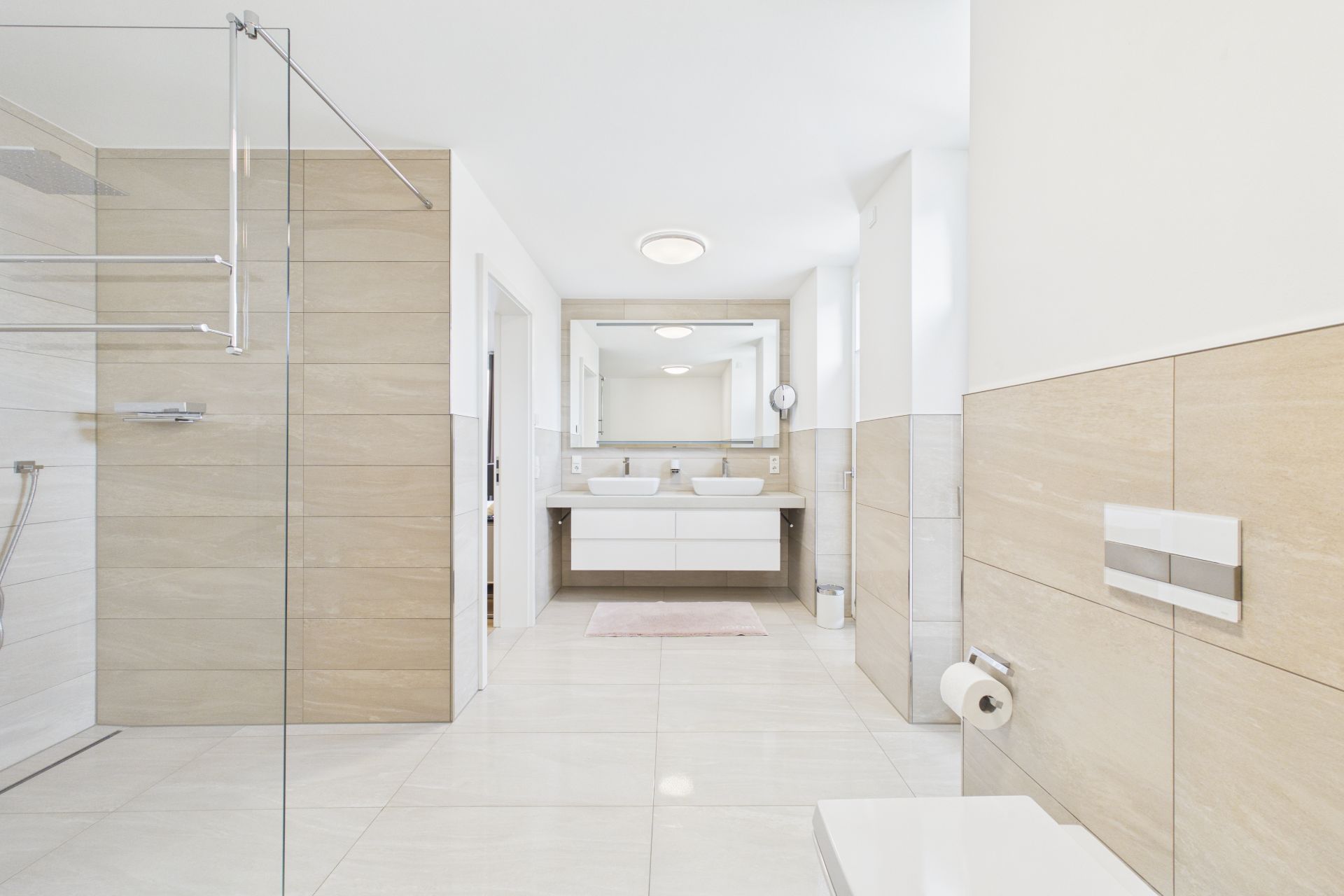 Modernes Badezimmer mit Doppelwaschbecken, Glasdusche und beigen Fliesen.