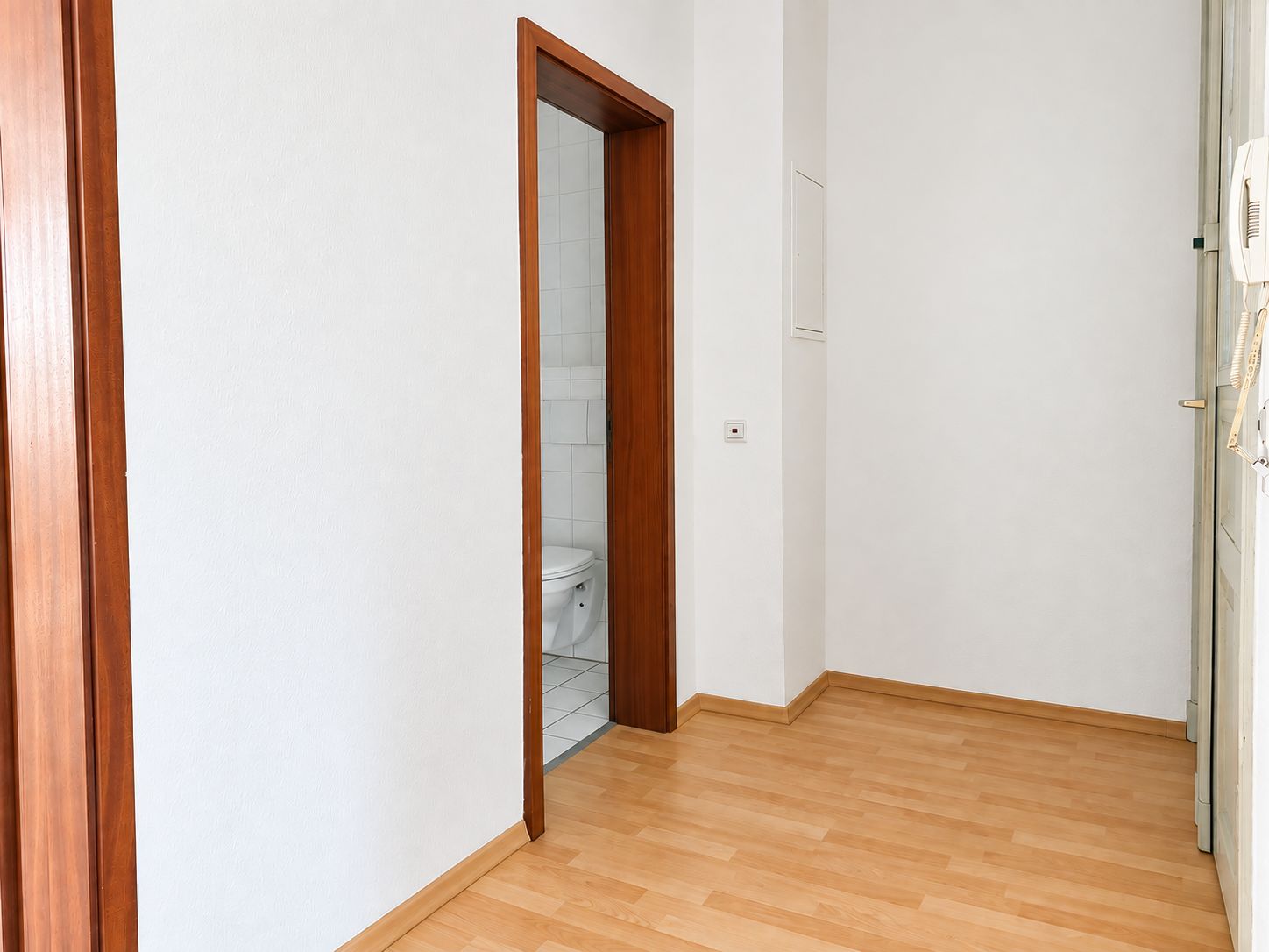 Flur mit hellem Laminatboden und Blick in ein Badezimmer mit weißer Keramiktoilette.