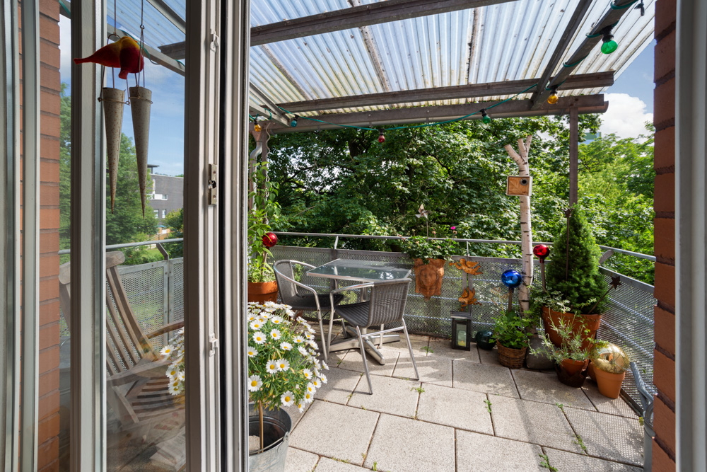 Balkon mit Tisch, Stühlen, Pflanzen und Überdachung, umgeben von viel Grün.