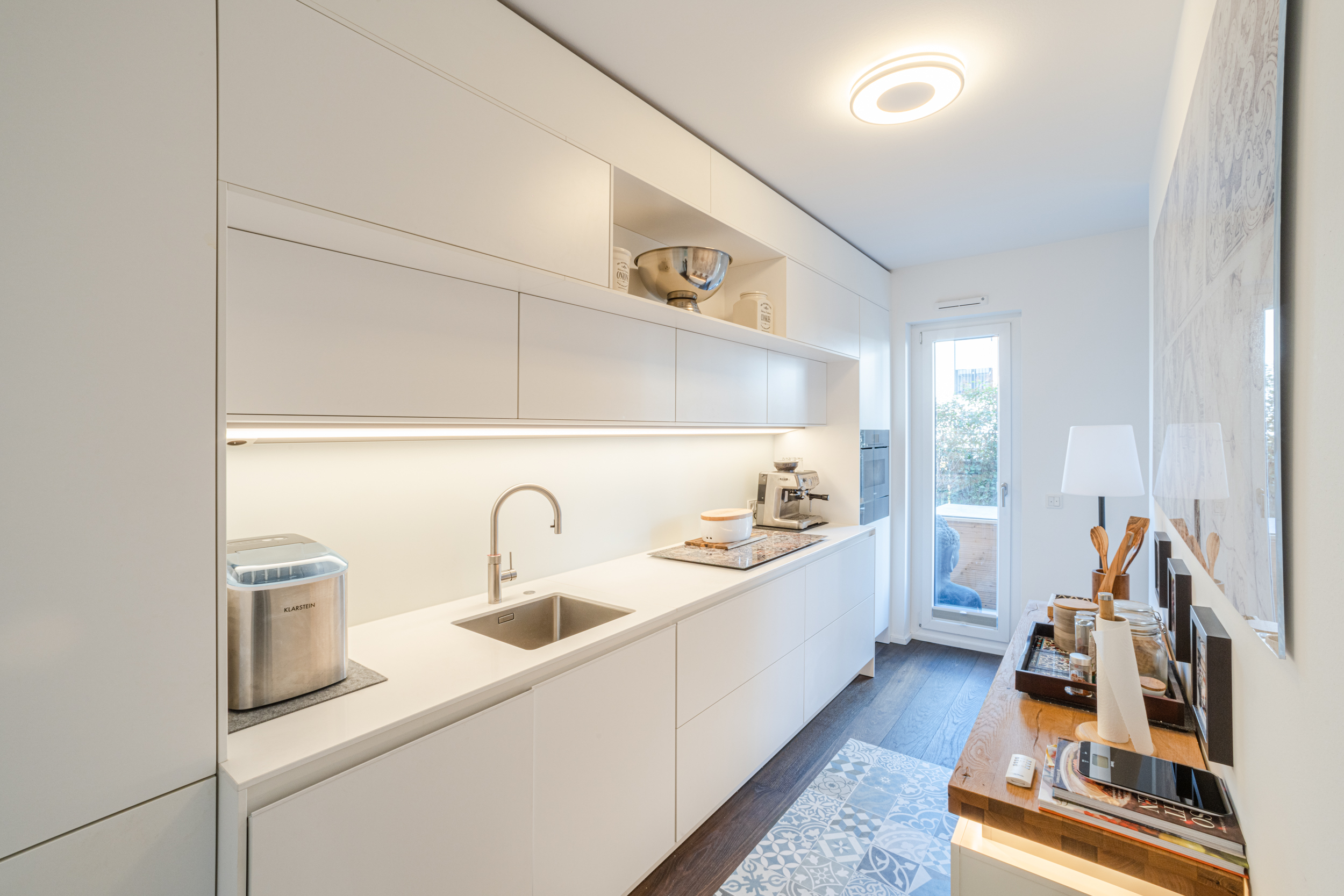 Moderne, helle Einbauküche mit weißen Schränken und Küchengeräten, Tür zum Balkon.