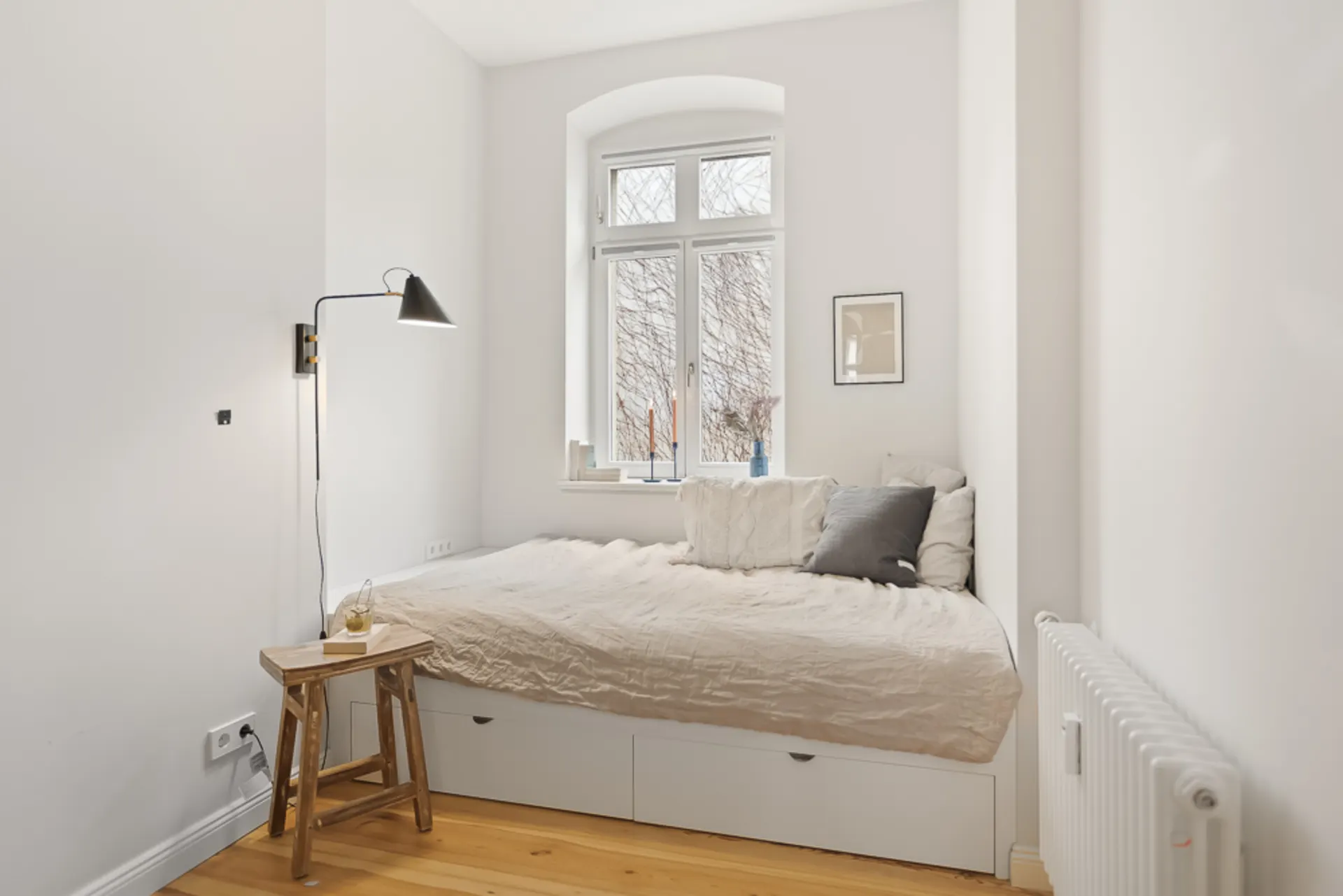 Kleines Schlafzimmer mit Bett, Stehlampe, Holzstuhl und Fenster mit Blick nach draußen.