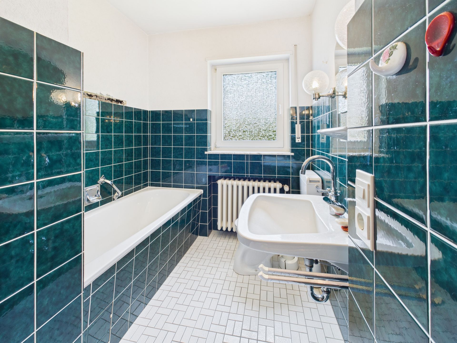 Helles Badezimmer mit Badewanne, Waschbecken, Fenster und grünen Fliesen.