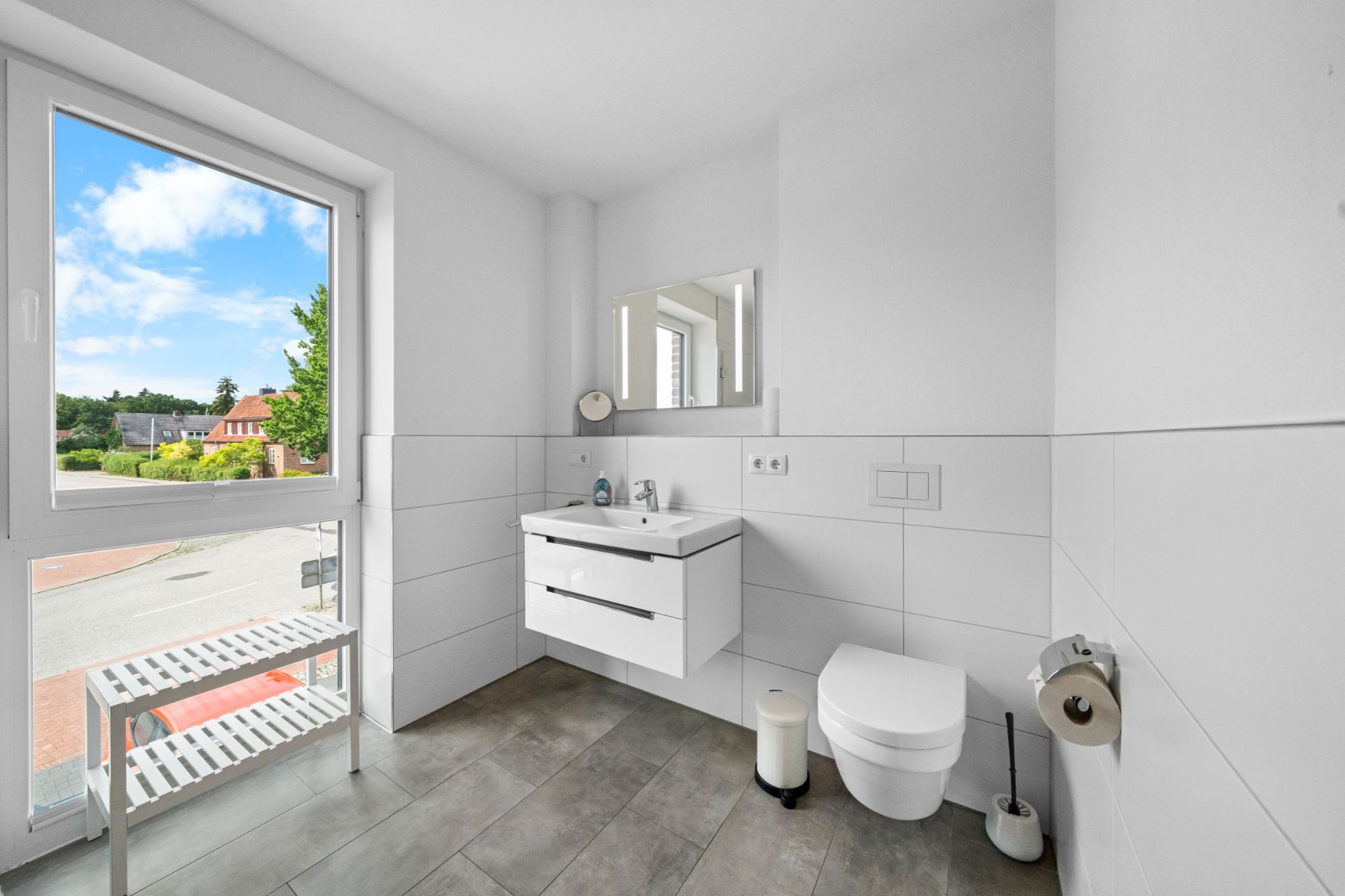 Modernes Badezimmer mit Fenster, Waschbecken, Spiegel und Wandtoilette.