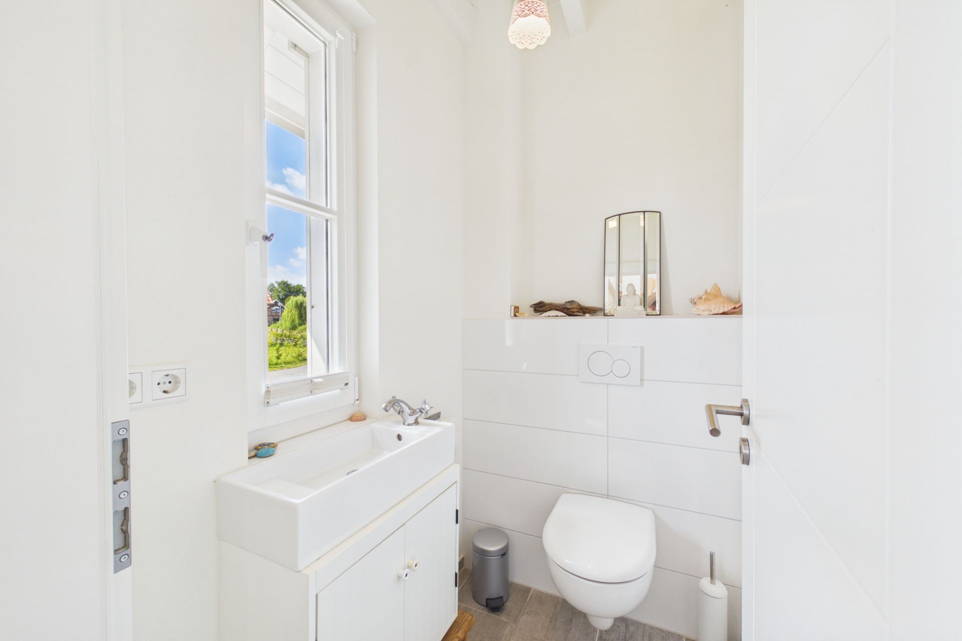 Helles Badezimmer mit Wandtoilette, Waschbecken, Fenster und Spiegel.