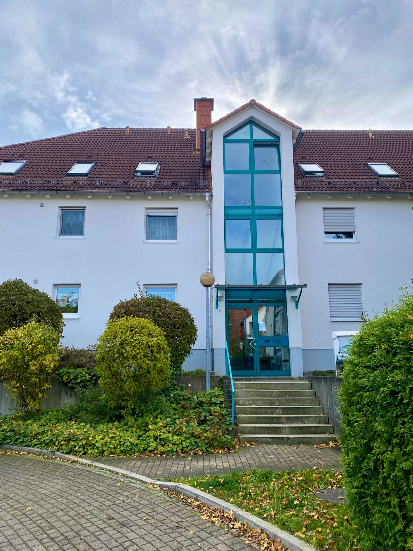 Eingang eines Wohnhauses mit Glasfront, Treppe und umliegenden Büschen.