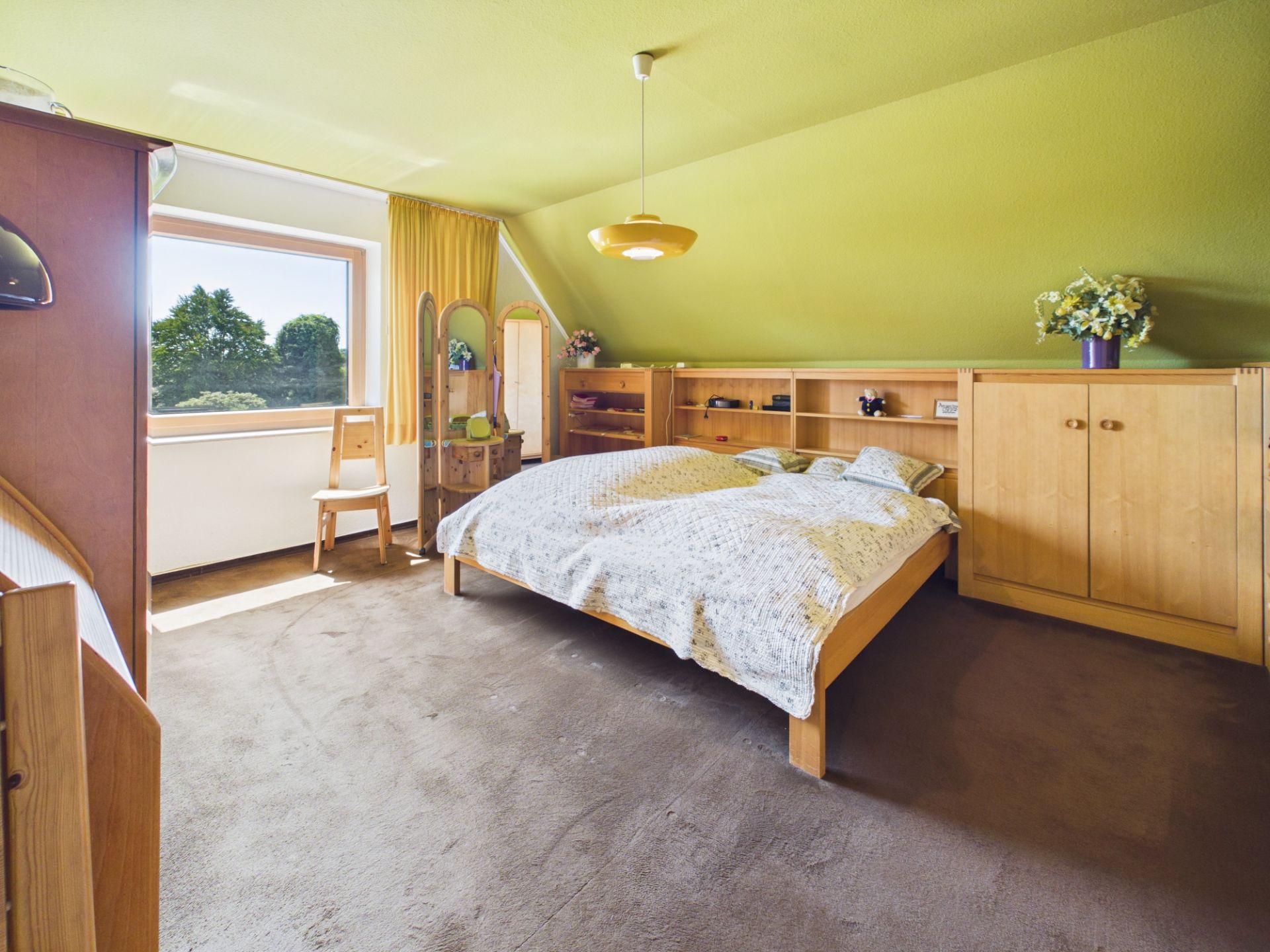 Helles Schlafzimmer mit Doppelbett, Holzschränken, Schminktisch und großem Fenster.