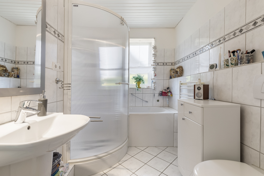 Helles Badezimmer mit Dusche, Badewanne, Waschbecken und Fenster.