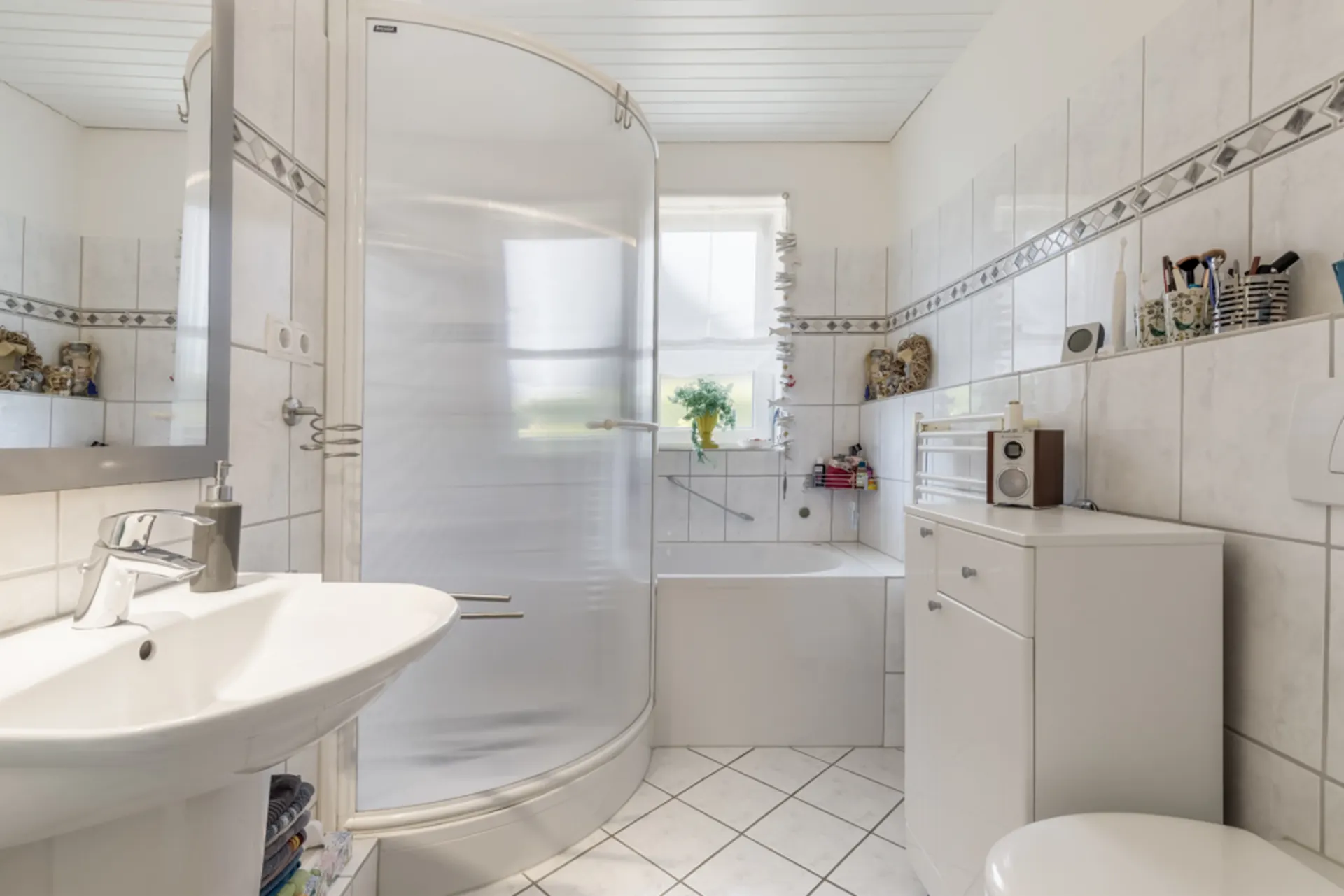 Helles Badezimmer mit Dusche, Badewanne, Waschbecken und Fenster.