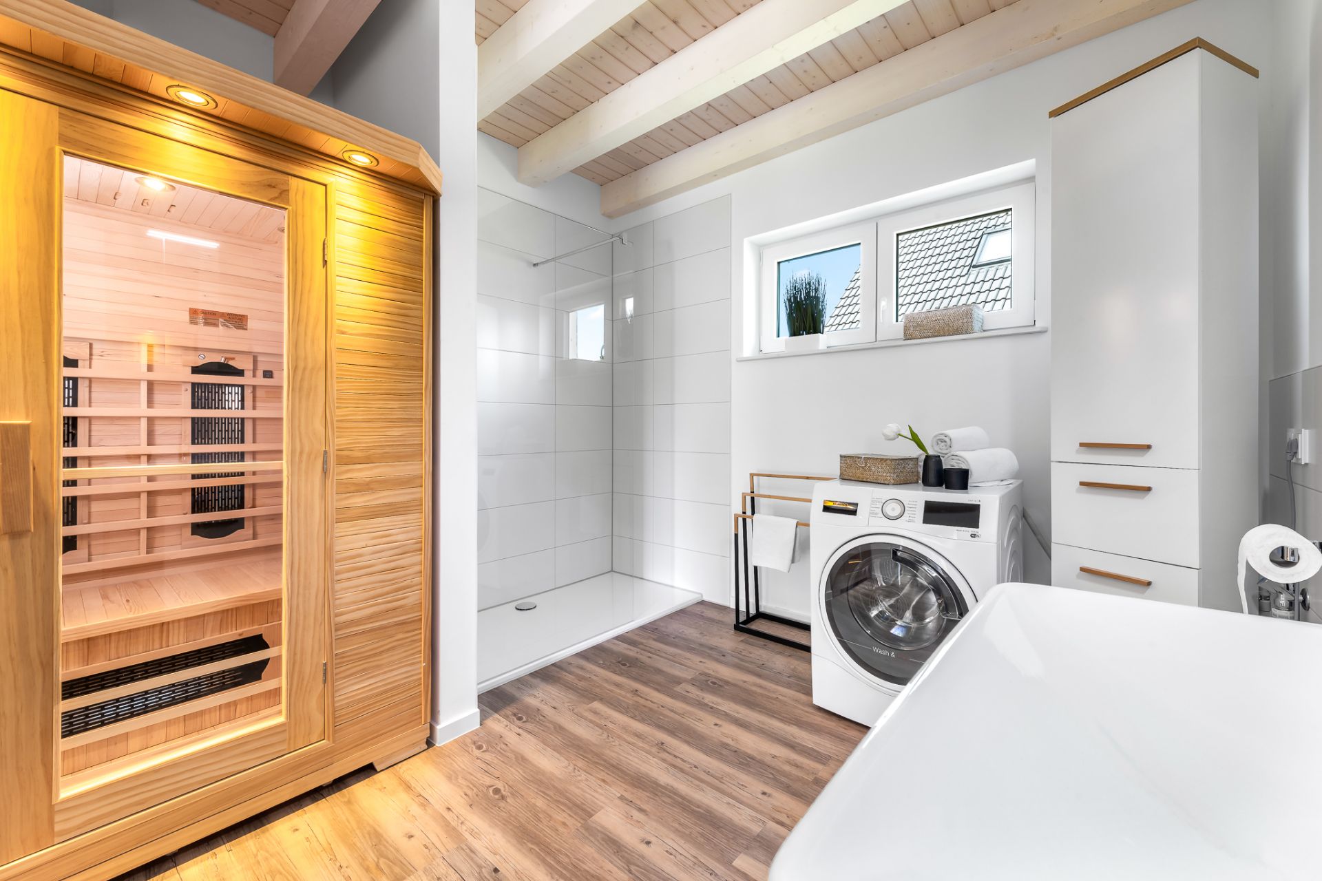 Modernes Badezimmer mit Sauna, Dusche, Waschmaschine und Holzfußboden.