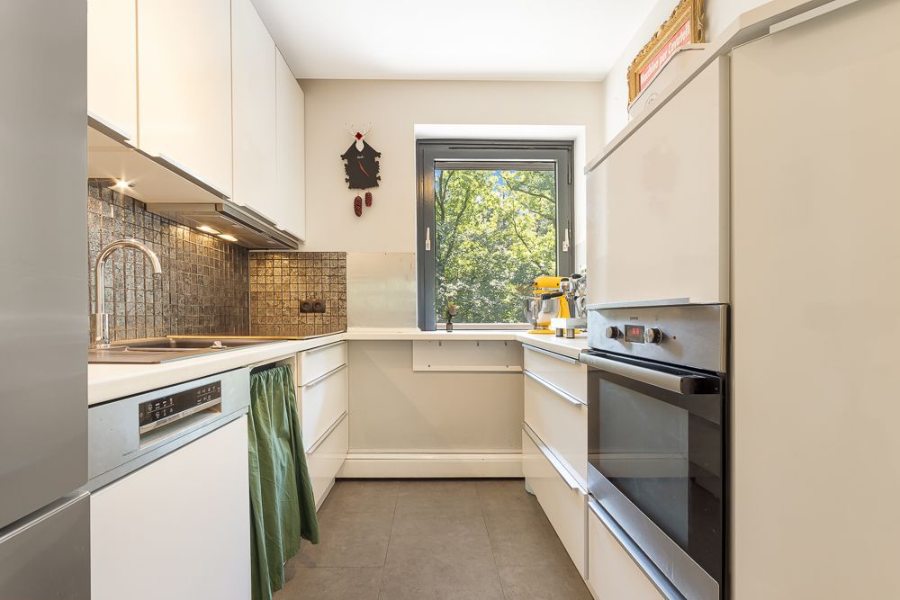 Moderne Küche mit weißen Schränken, backofen und Fenster mit Blick ins Grüne.