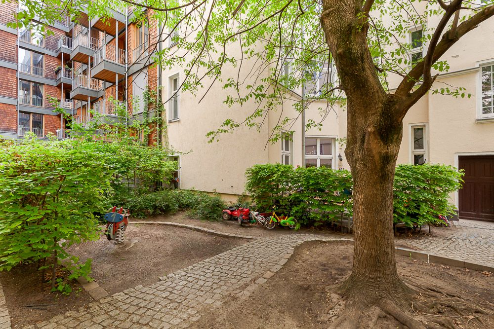 Innenhof mit Baum, Kopfsteinpflasterweg, Büschen und einigen Kinderspielzeugen.