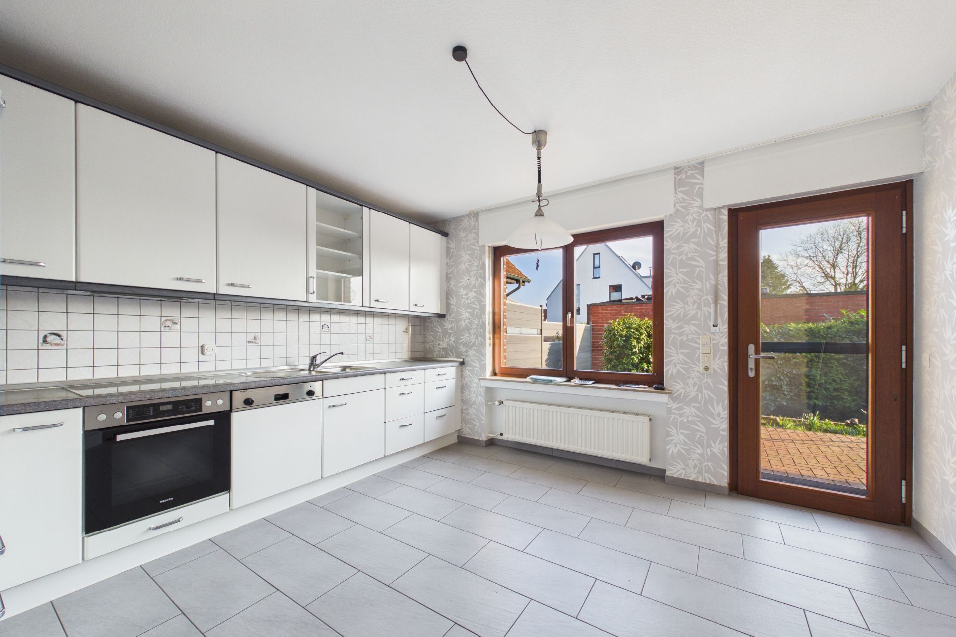 Helle Küche mit weißen Schränken, Fenster und Tür zum Garten.