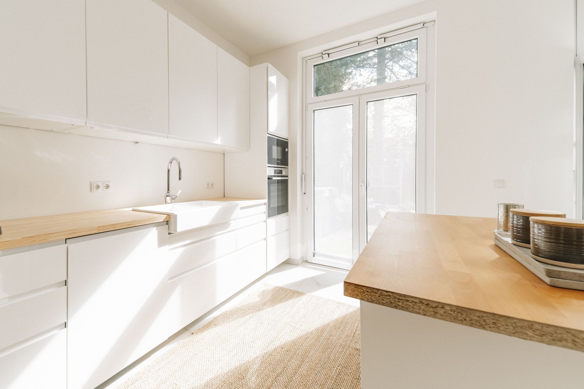 Helle, moderne Küche mit weißen Schränken, Holzarbeitflächen und großem Fenster mit Glastür.