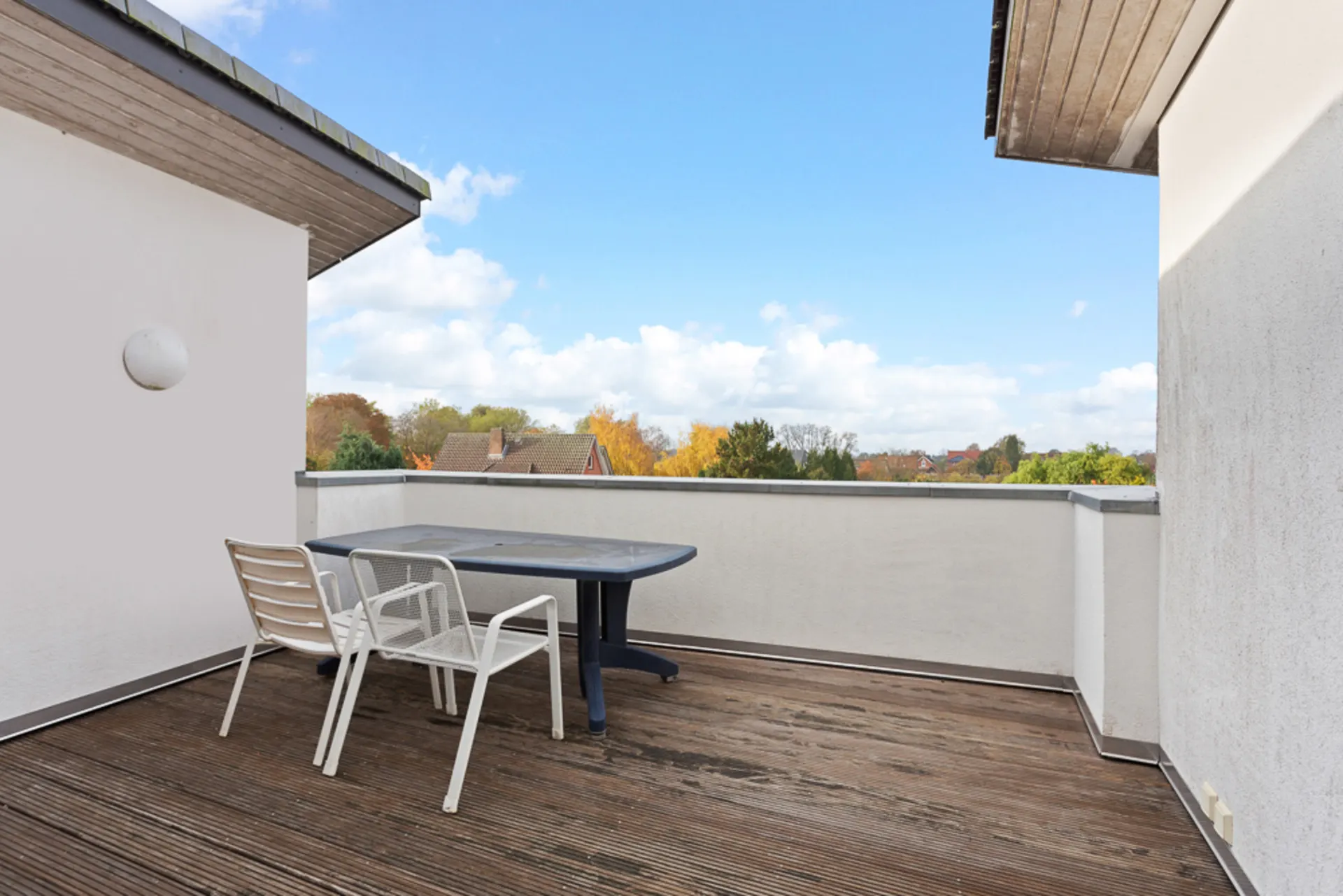 Geräumiger Balkon mit Holzboden, Tisch und zwei weißen Stühlen, umgeben von weißem Geländer.