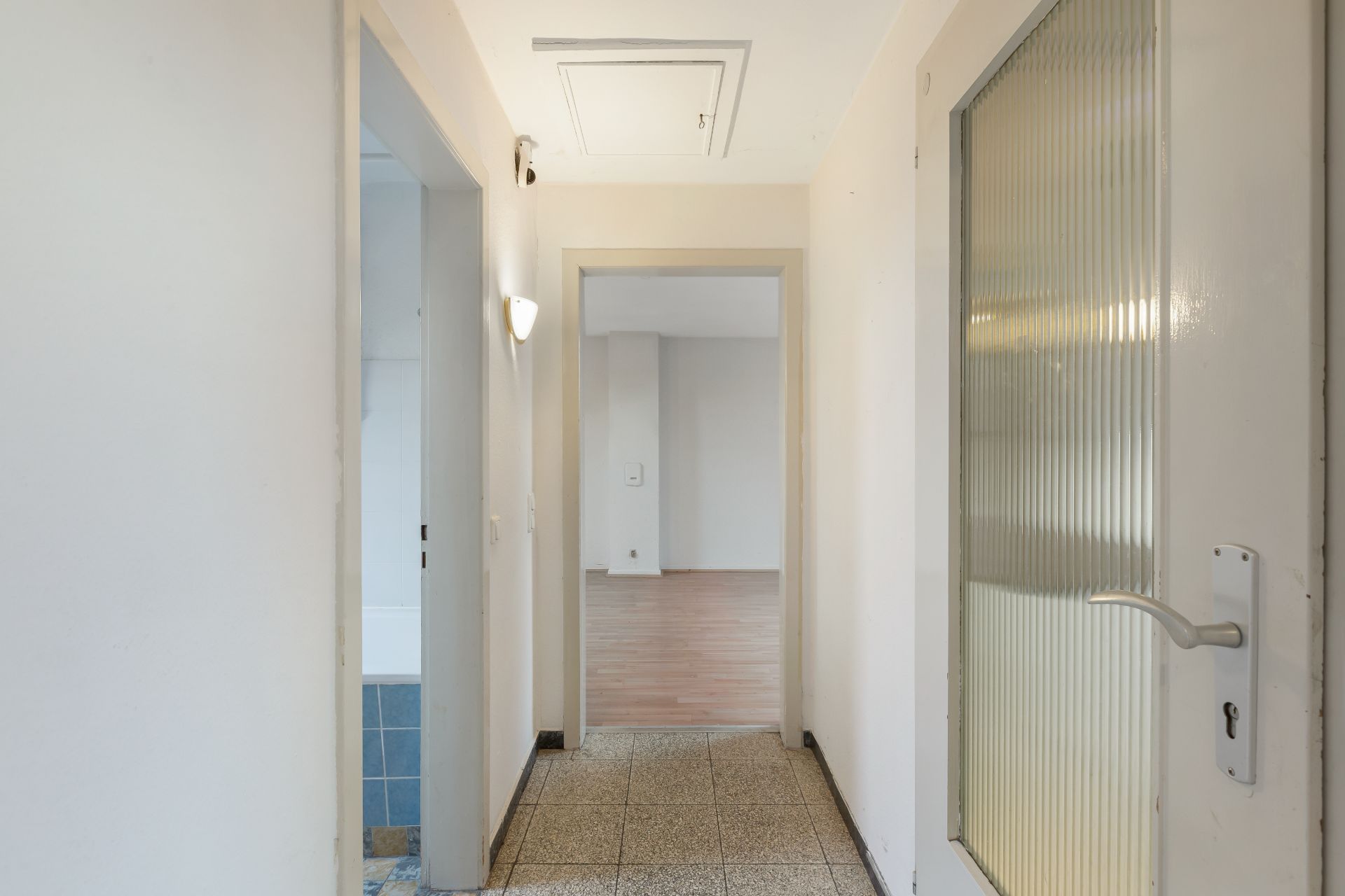 Heller Flur mit Türen, Fliesenboden und Blick in ein Zimmer mit Parkett.