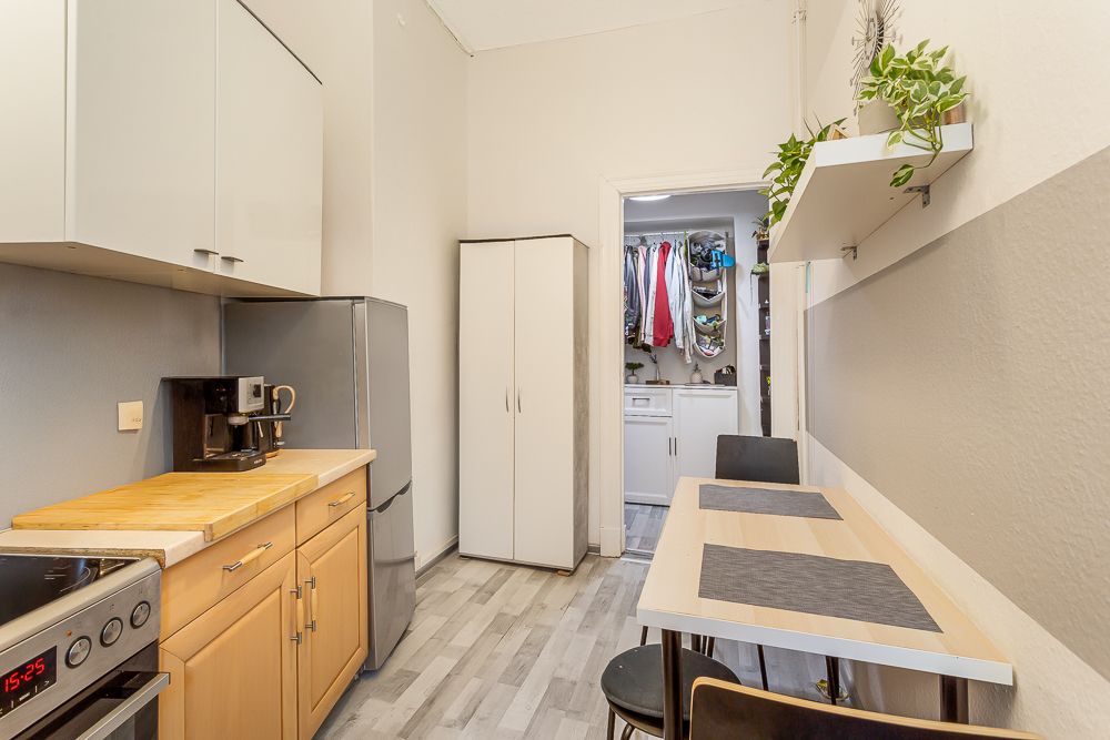 Helle Küche mit Esstisch, Kühlschrank, Kaffeeautomat und Blick in einen Hauswirtschaftsraum mit Waschmaschine.