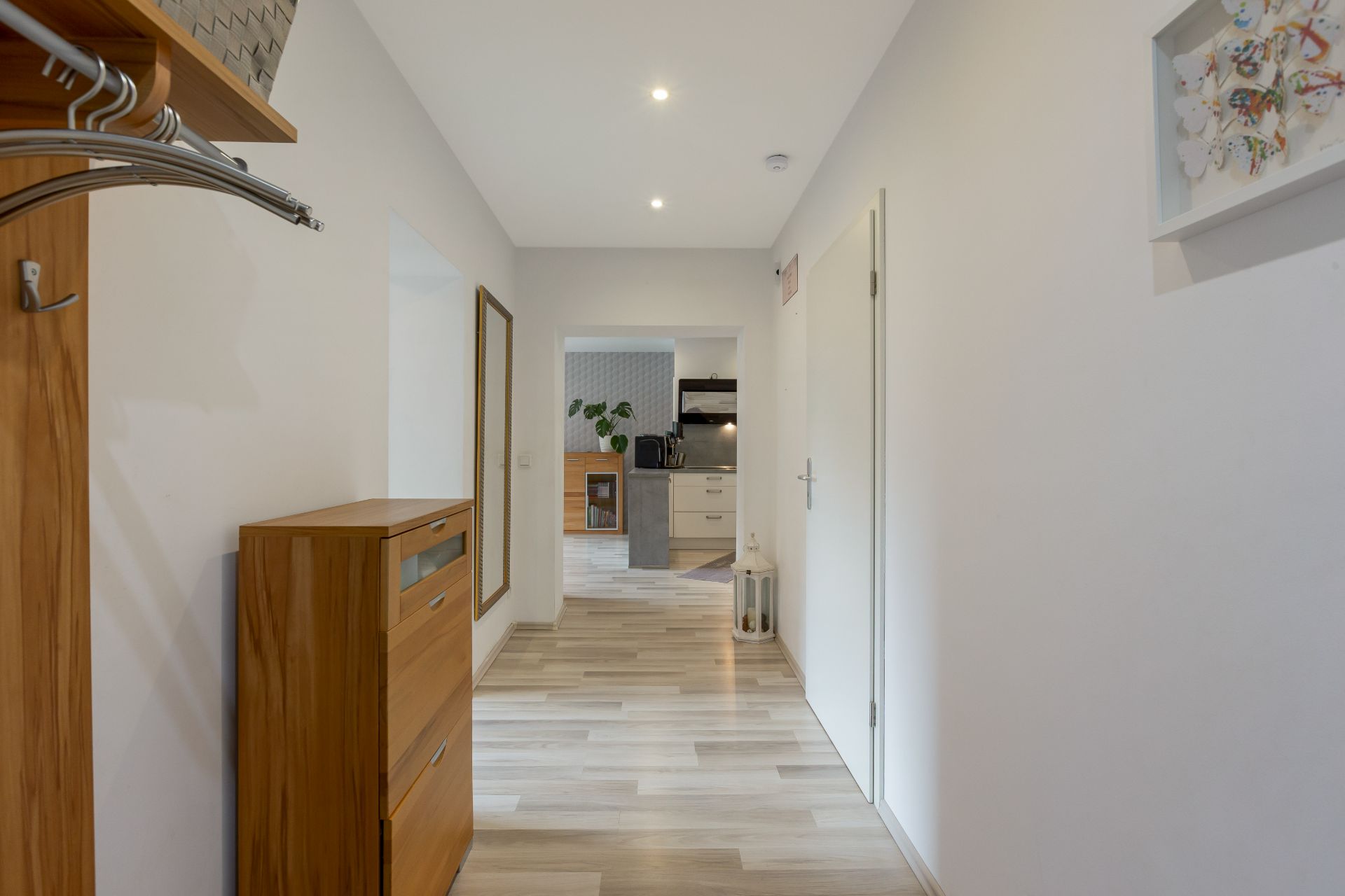 Heller Flur mit Holzkommode, Garderobe, Spiegel und Blick in eine Küche.
