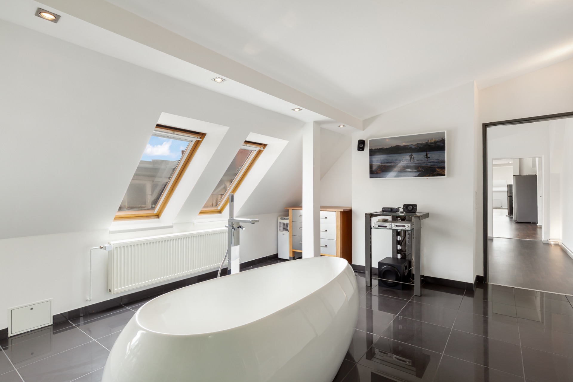 Modernes Badezimmer mit freistehender Badewanne, Dachfenstern und glänzendem Fliesenboden.