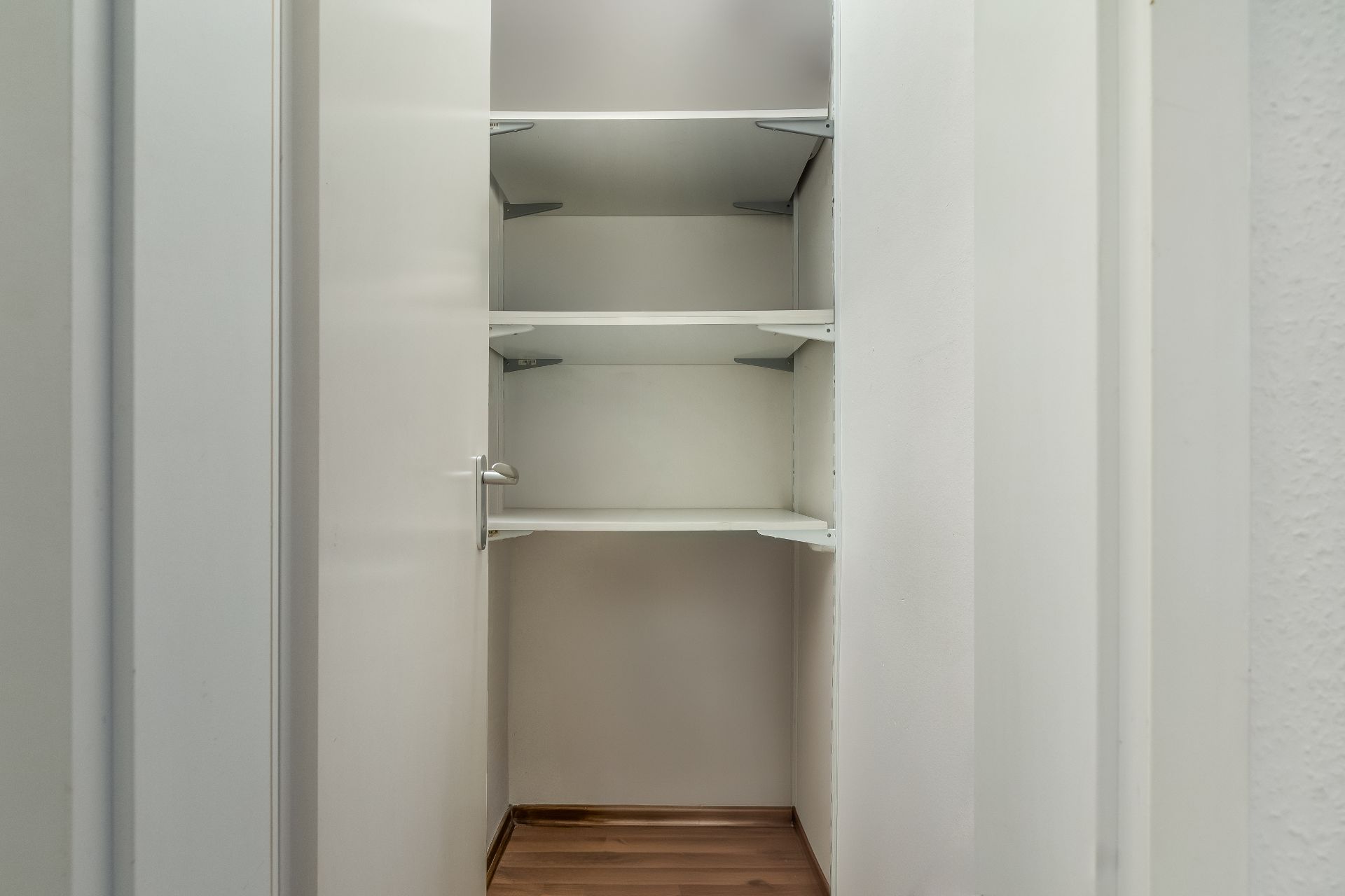Geöffneter Einbauschrank mit mehreren weißen Regalböden und Holzboden.