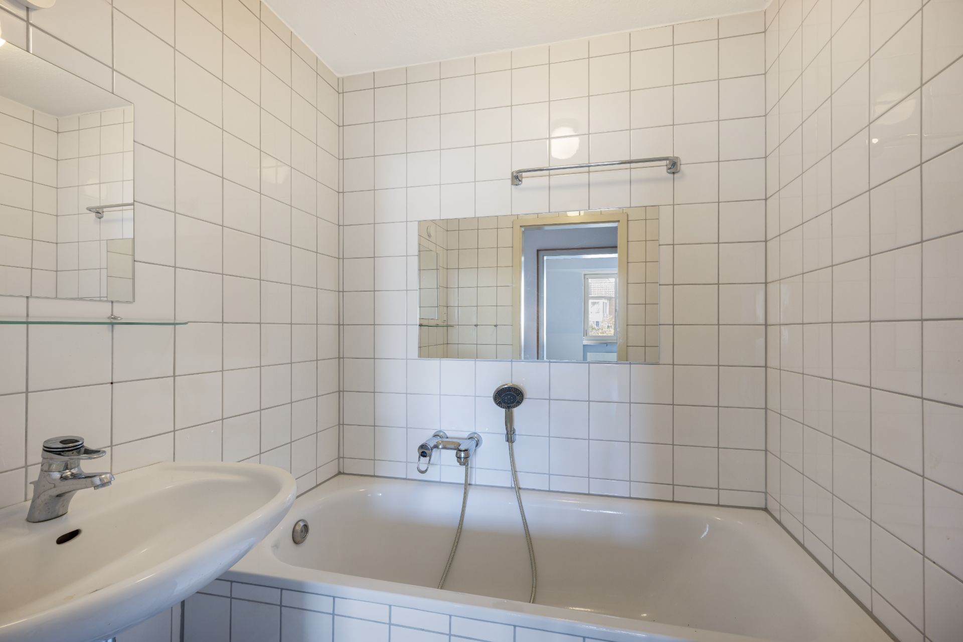 Bad mit weiß gefliesten Wänden, Waschbecken, Badewanne und Spiegel.