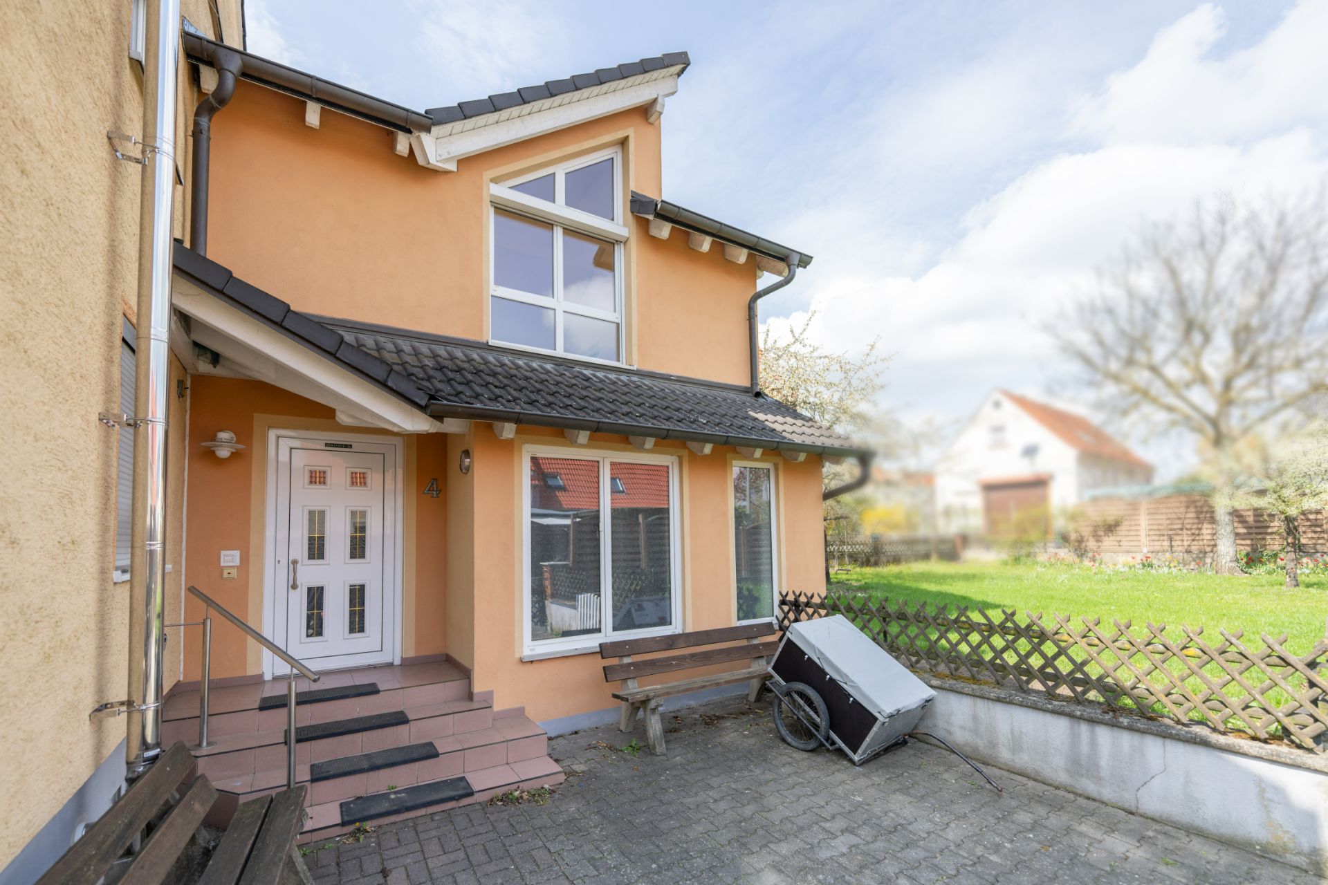 Eingangsbereich eines Hauses mit Treppe, Bank und Garten im Hintergrund.