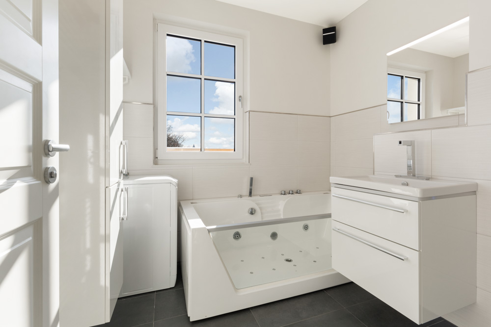 Modernes weißes Badezimmer mit großer Badewanne, Waschbecken und Fenster.