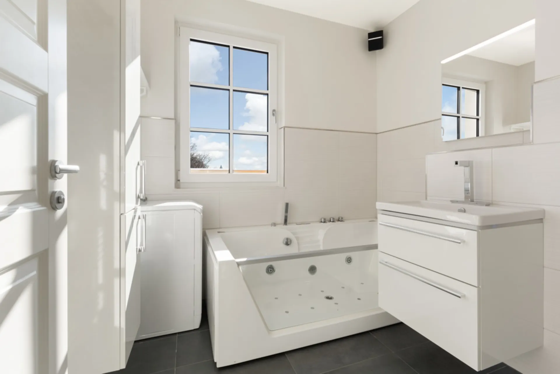 Modernes weißes Badezimmer mit großer Badewanne, Waschbecken und Fenster.
