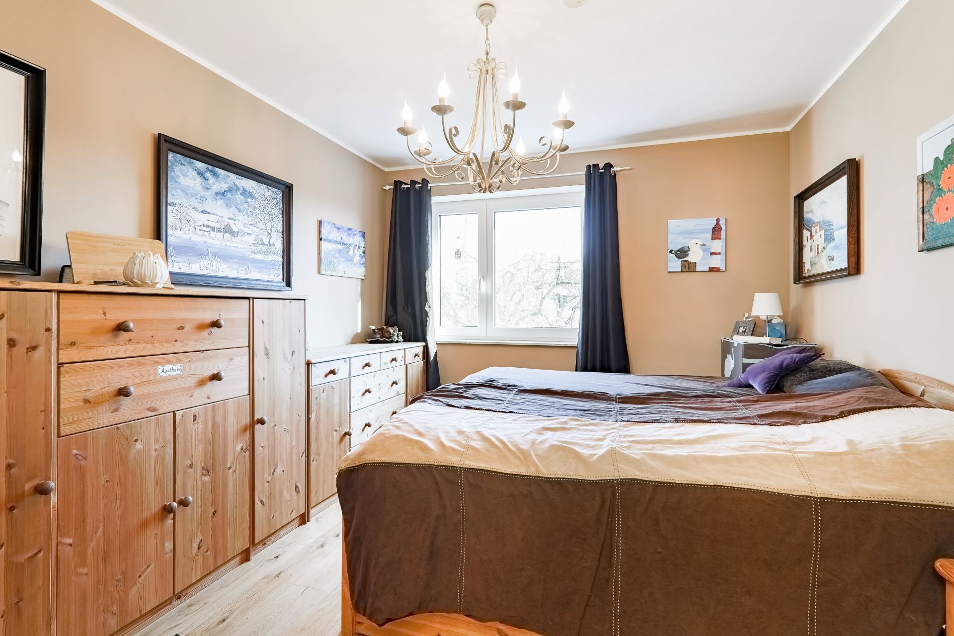 Schlafzimmer mit Holzmöbeln, großem Bett, Fenster und mehreren Bildern an den Wänden.