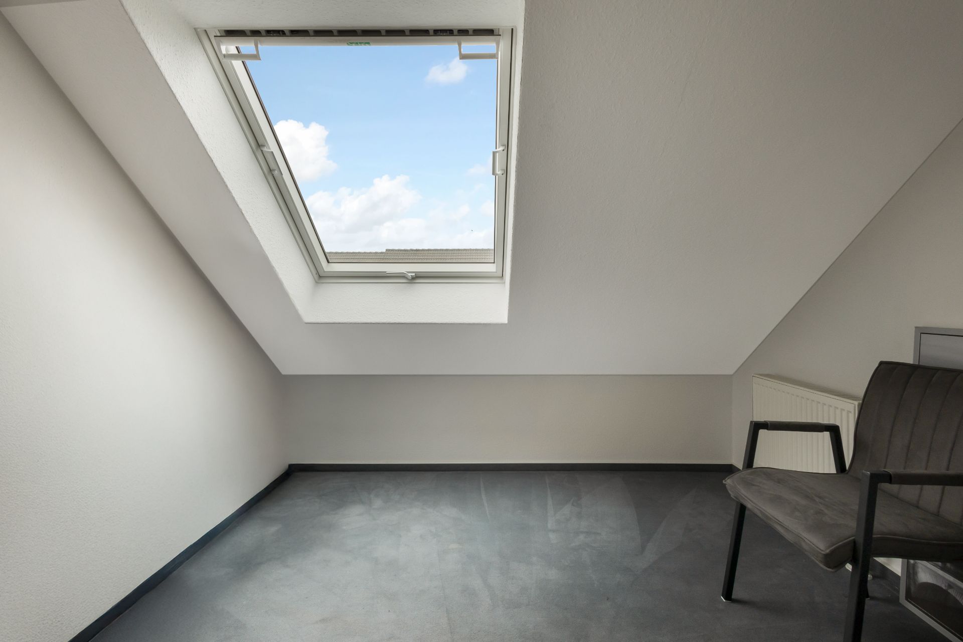 Heller Raum mit Dachfenster, grauem Boden und einem Stuhl in der Ecke.