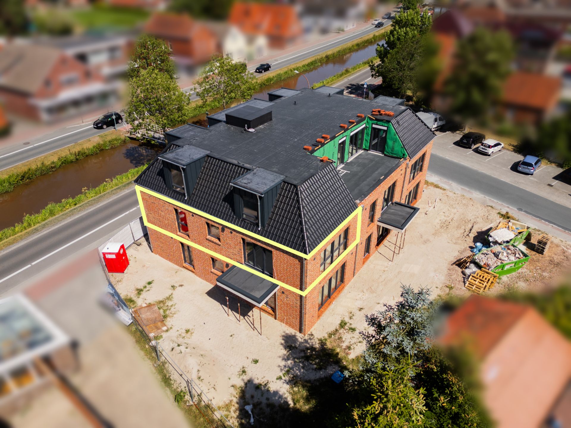 Neubau eines Mehrfamilienhauses mit dunklem Dach und großen Fenstern an einer Straßenecke.