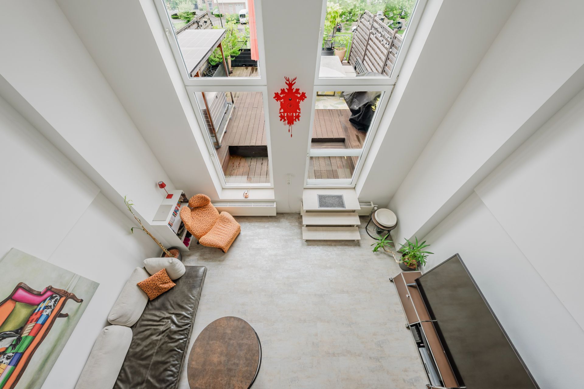 Wohnzimmer mit großen Fenstern, Sofa, Sessel, Couchtisch und Zugang zur Terrasse, von oben gesehen.
