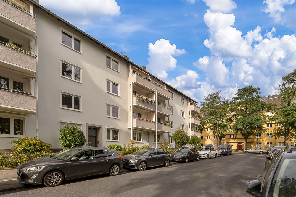 Mehrfamilienhaus mit Balkonen und geparkten Autos an einer ruhigen Wohnstraße.